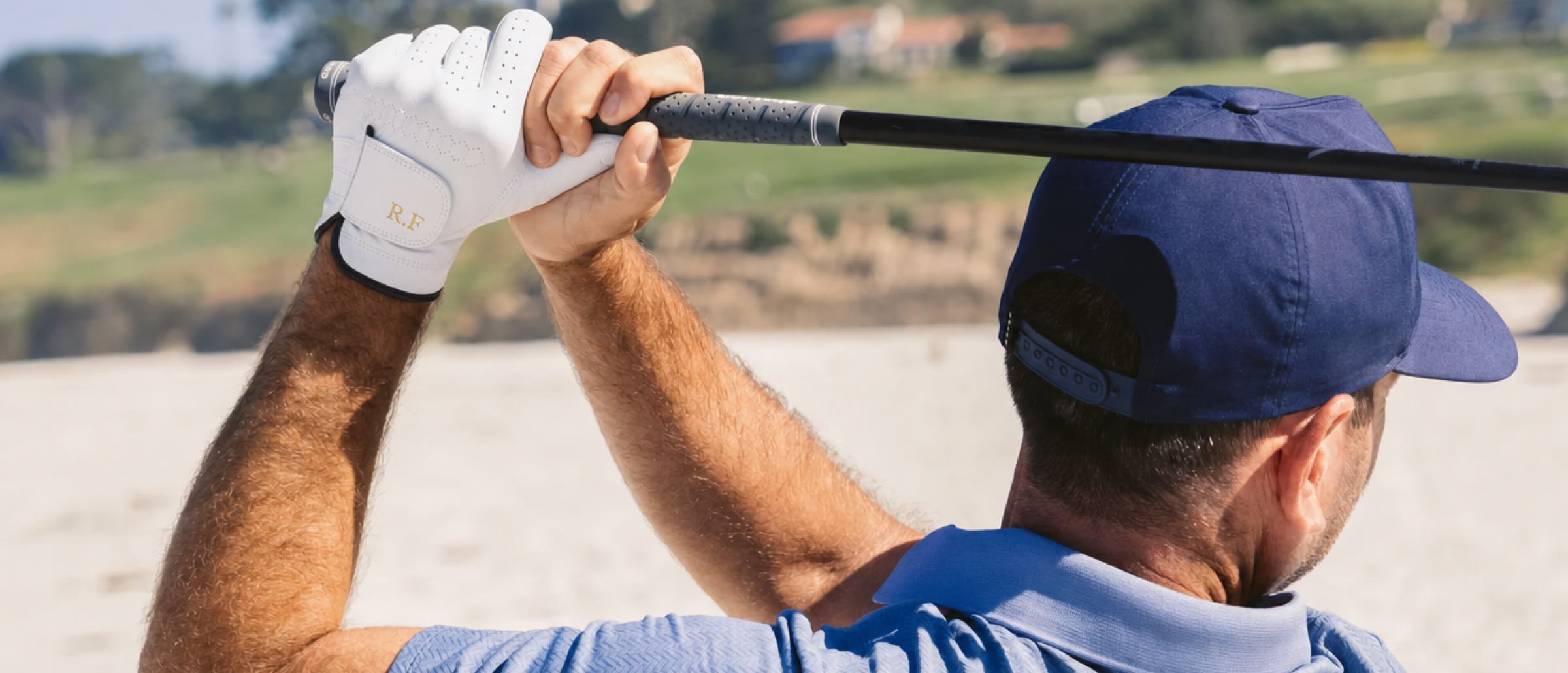 A golfer at the top of his swing in the white Monogram Glove, initials R.F in gold foil on the strap.